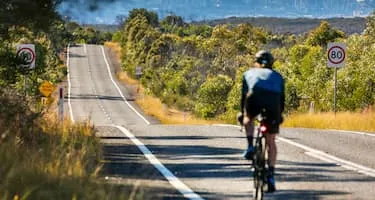 A cyclist rides downhill, passing green bushland on the road towards Sydney, New South Wales.