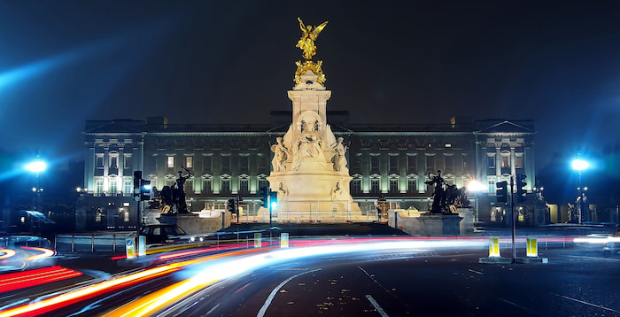 Evening time lapse of car lights swirling past Queen Victoria Monument in front of Buckingham Palace with lights illuminating the architecture.